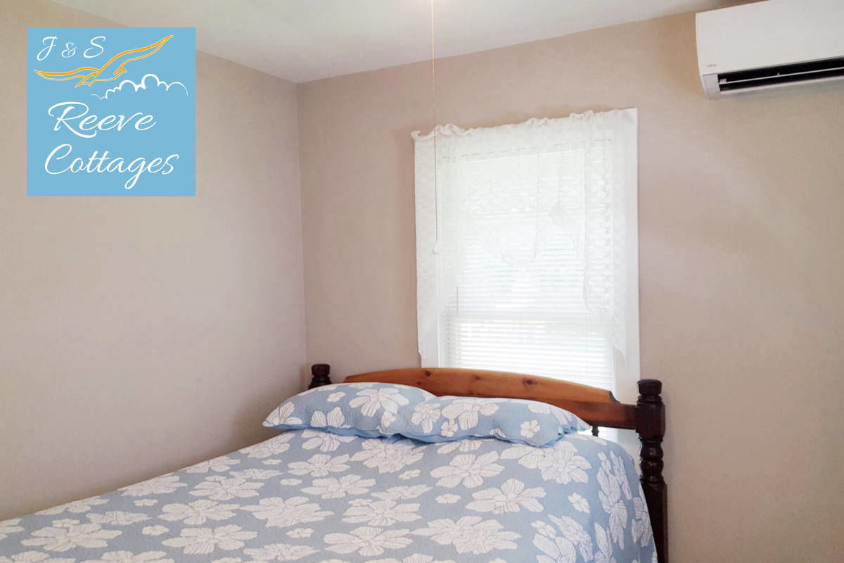 Cozy Waterfront Cottage 5 shows bedroom one with queen bed, dresser, wall mount air conditioning and heat